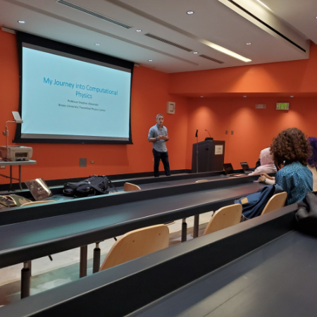 Instructor presenting “My Journey into Computational Physics” to a small group of students in a classroom with tiered seating and a projection screen.
