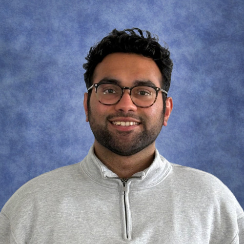 Smiling young man with glasses wearing a zip-neck white sweater.