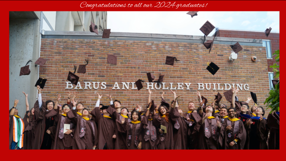 Graduates toss their caps in the air under the barus and holley sign.